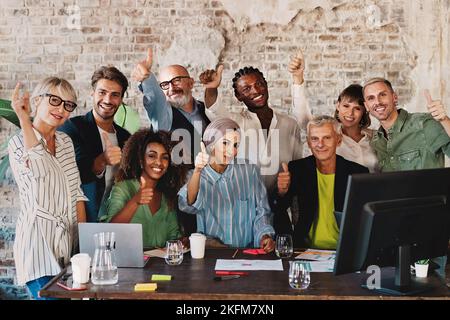 Multi-ethnic group of coworkers in thumbs-up pose sitting at office desk - Portrait of business colleagues excited for success - Business lifestyle co Stock Photo
