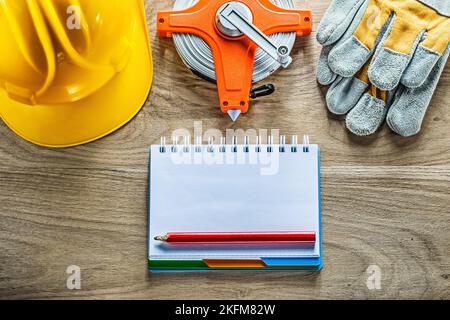 Notebook pencil safety gloves tape measure hard hat on wooden board. Stock Photo