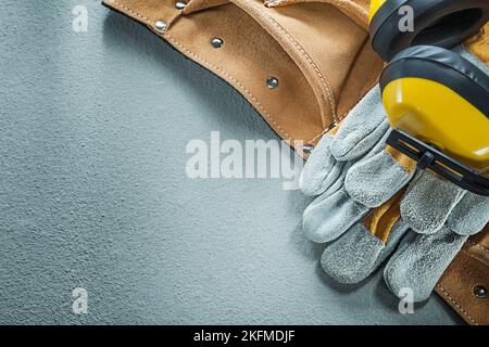 Set of leather tool belt safety gloves earmuffs on concrete background. Stock Photo