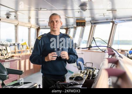 Deck officer with binoculars on navigational bridge. Seaman on board of vessel. Commercial shipping. Cargo ship. Stock Photo