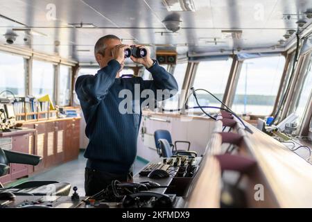 Deck officer with binoculars on navigational bridge. Seaman on board of vessel. Commercial shipping. Cargo ship. Stock Photo