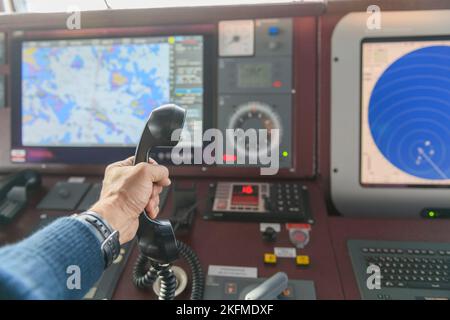 Navigational control panel and VHF radio with hand. Radio communication at sea. Working on the ship's bridge. Stock Photo