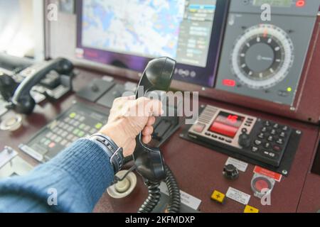 Navigational control panel and VHF radio with hand. Radio communication at sea. Working on the ship's bridge. Stock Photo