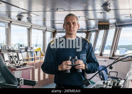 Deck officer with binoculars on navigational bridge. Seaman on board of vessel. Commercial shipping. Cargo ship. Stock Photo