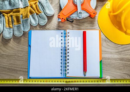 Spiral notebook pencil protective gloves measuring tape building helmet on wooden board. Stock Photo