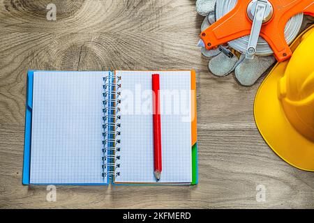 Spiral notebook pencil protective gloves tape measure building helmet on wooden board. Stock Photo