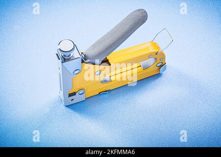 Yellow metal construction stapler on blue background top view. Stock Photo