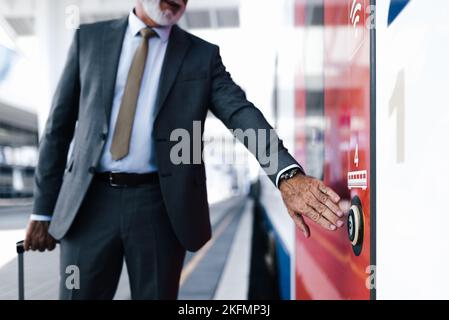 Midsection of businessman pushing open door button of subway train. Senior male professional is standing at station platform. He is wearing suit durin Stock Photo