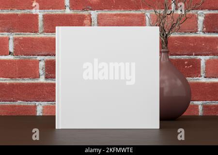 Square book cover mock up standing on a dark wooden desk with red brick wall background Stock Photo