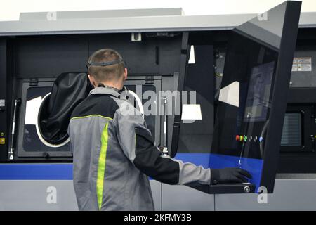 The worker controls workflow inside large industrial 3D printer printing metal powder standing near worker's control panel. The working process. Industrial powder 3d printer for metal and worker man. Stock Photo