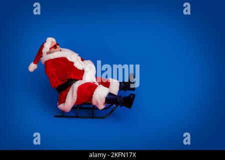 Full size profile photo of funny santa go by sled wear cap glasses coat pants shoes isolated on red color background Stock Photo