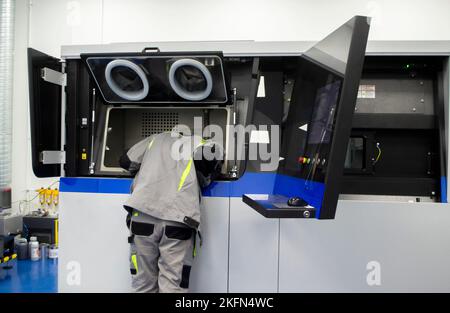 A worker looks into open window of inside large industrial 3D printer for metal powder. The working process. Industrial powder 3d printer for metal and worker man. Laser sintering machine for metal. Stock Photo