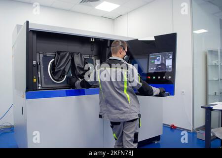 The worker controls workflow inside large industrial 3D printer printing metal powder standing near worker's control panel. The working process. Industrial powder 3d printer for metal and worker man. Stock Photo