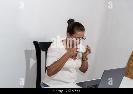 Older Woman Drinking A Cup Of Coffee While Using Laptop. Stock Photo