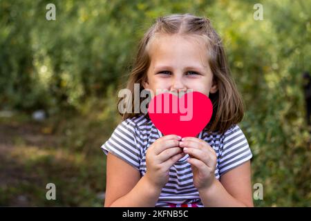 A child with a paper heart in his hands. Congratulations on Valentine's Day. copy space. Portrait of a cute little girl in the park outdoors. Love Stock Photo