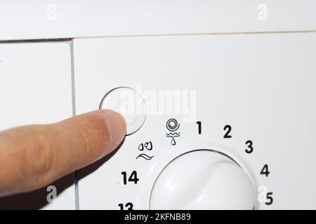 Man's hand presses the buttons on the control panel of the washing machine Stock Photo