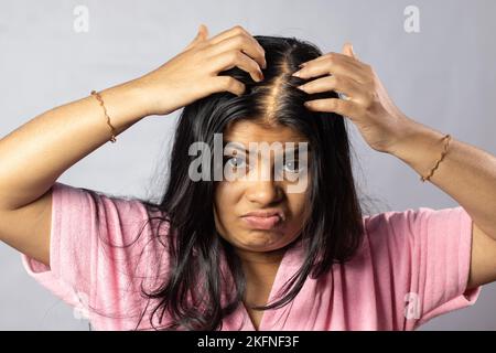 An Indian woman worried due to hair loss problem holds scalp on white background Stock Photo