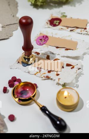 The process of creating wedding place cards from homemade recycled paper, pressed flowers and sealing wax. Personalized wedding name tags. Stock Photo