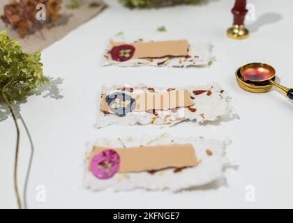 The process of creating wedding place cards from homemade recycled paper, pressed flowers and sealing wax. Personalized wedding name tags. Stock Photo