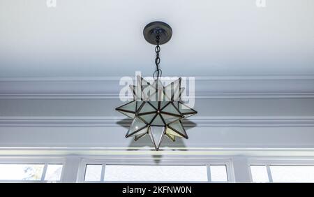 A metal and glas star shaped hanging lighting fixture near a large kitchen window Stock Photo