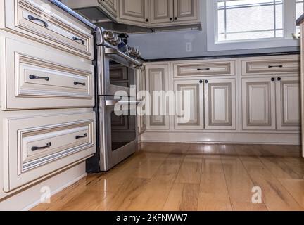 A low angle view of rustic cream colroed light kitchen cabinets in a new construction house with wood floors Stock Photo