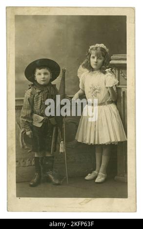 Original charming postcard of children in fancy dress costumes - the girl (age 7) called Connie Millar is dressed up as a fairy and shows the photographer her doll (but looks bored) and her brother (age 5) Willie Millar wears a boy Scout's uniform and is carrying a flag with the Latin for God Save the King (Vivat Rex) and a Scout axe -. From  E. Van Trolga's studios either at Putney or Clapham (London) U.K. dated 1912. Stock Photo