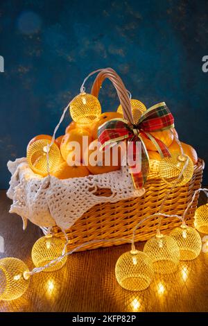 Tangerines and garlands lie in a basket on a blue background. There is a red bow on the basket. Stock Photo