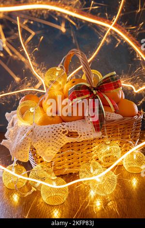Tangerines and garlands lie in a basket on a blue background. In the photo, the light lines of sparklers. There is a red bow on the basket. Stock Photo