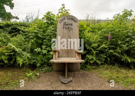 A wooden bench at the start of the Faerie Trail in Loch Lomond, Scotland. Loch Lomond Faerie Trail Chair / Bench Stock Photo