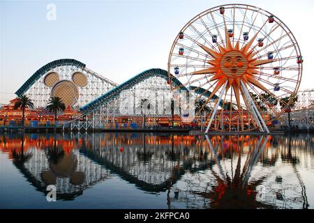 The Ferris Wheel and roller coaster of an amusement park are reflected in the calm water of Disneyland California Adventure Stock Photo