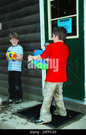 Two young boys enjoy a friendly water gun fight on a summer day outside of their cabin in the summer Stock Photo