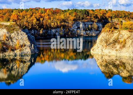 A gorgeous landscape with a tranquil lake reflecting cliffs and vibrant autumnal trees under a cloudy sky Stock Photo