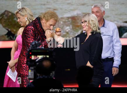 Friedrichshafen, Germany. 19th Nov, 2022. Excavator driver Sandra Hasenauer gets a kiss on the hand from Thomas Gottschalk after winning her excavator weather on the ZDF show 'Wetten, dass.?' with Thomas Gottschalk and Michelle Hunziker. After the successful comeback in November 2021, there will also be a revival of the legendary ZDF Saturday night show in 2022. Credit: Philipp von Ditfurth/dpa/Alamy Live News Stock Photo