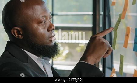 Middle-aged african american ethnic man businessman developer manager boss designer work in modern office stand near glass wall read sticker notes Stock Photo