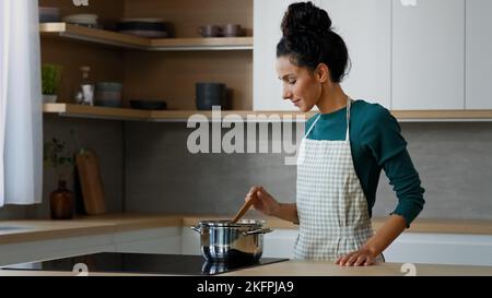 Female chef arabian woman cooker wife mother cooking aromatic dish on stove at home kitchen preparing healthy food with fresh natural ingredients stir