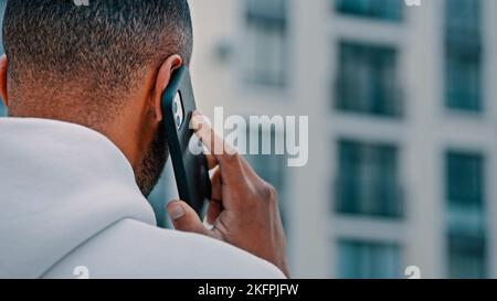 Rear view african man adult latina freelancer speak cellphone outdoor city street talk phone mobile distant conversation use free wifi outside modern Stock Photo