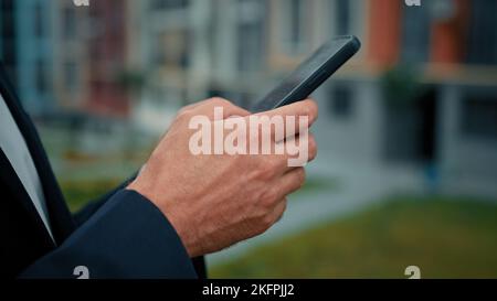 Unknown millennial man entrepreneur standing outside holding in hands modern gadget using mobile device for business communication online texting Stock Photo