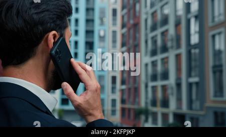 Rear back view businessman talk mobile phone outside on city street use wireless cell connection distance call discuss remote business deal with Stock Photo