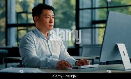 Professional male worker asian korean man successful businessman programmer specialist sit at office desk work with computer software program Stock Photo
