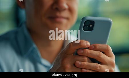 Unknown asian man businessman worker modern user senior entrepreneur hold in hands phone search online information use mobile business apps wifi 5g Stock Photo