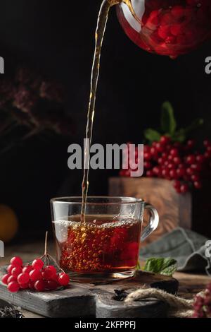 Viburnum tea is poured into a cup from a glass teapot with steam ...