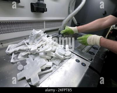 Man cleans details printed on industrial 3D printer from white plastic powder. Automated additive technologies. Person cleans vacuum cleaner plastic powder from models printed on 3D printer. Top view Stock Photo