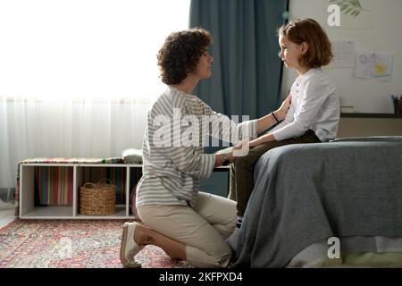 Young mother having conversation with her child while they sitting in bedroom Stock Photo