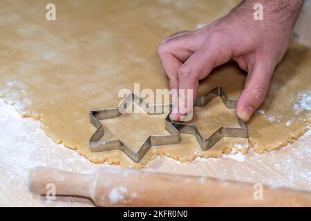 young man cutting the dough of cinnamon and vanilla star-shaped biscuits Stock Photo