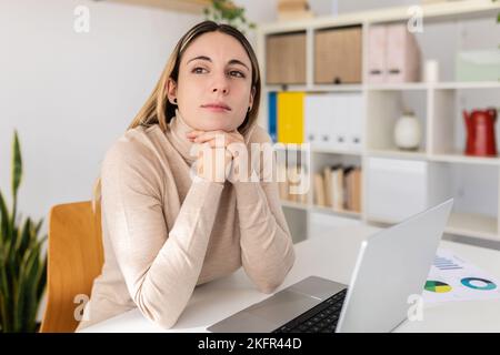 Young adult woman sitting at desk with laptop thinking about inspiration ideas Stock Photo