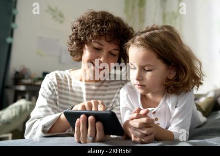 Smiling mother showing video on smartphone to her child during their leisure time at home Stock Photo