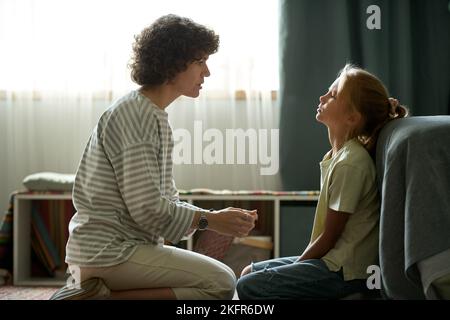 Young mother having conversation with her difficult daughter while they sitting in the room Stock Photo