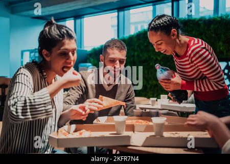 Eating pizza with diverse colleagues in the office, happy multi-ethnic employees having fun together during lunch, enjoying good conversation, and Stock Photo