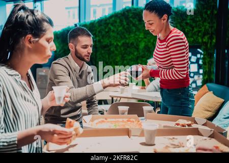 Eating pizza with diverse colleagues in the office, happy multi-ethnic employees having fun together during lunch, enjoying good conversation, and Stock Photo