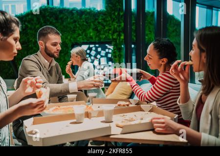 Eating pizza with diverse colleagues in the office, happy multi-ethnic employees having fun together during lunch, enjoying good conversation, and Stock Photo